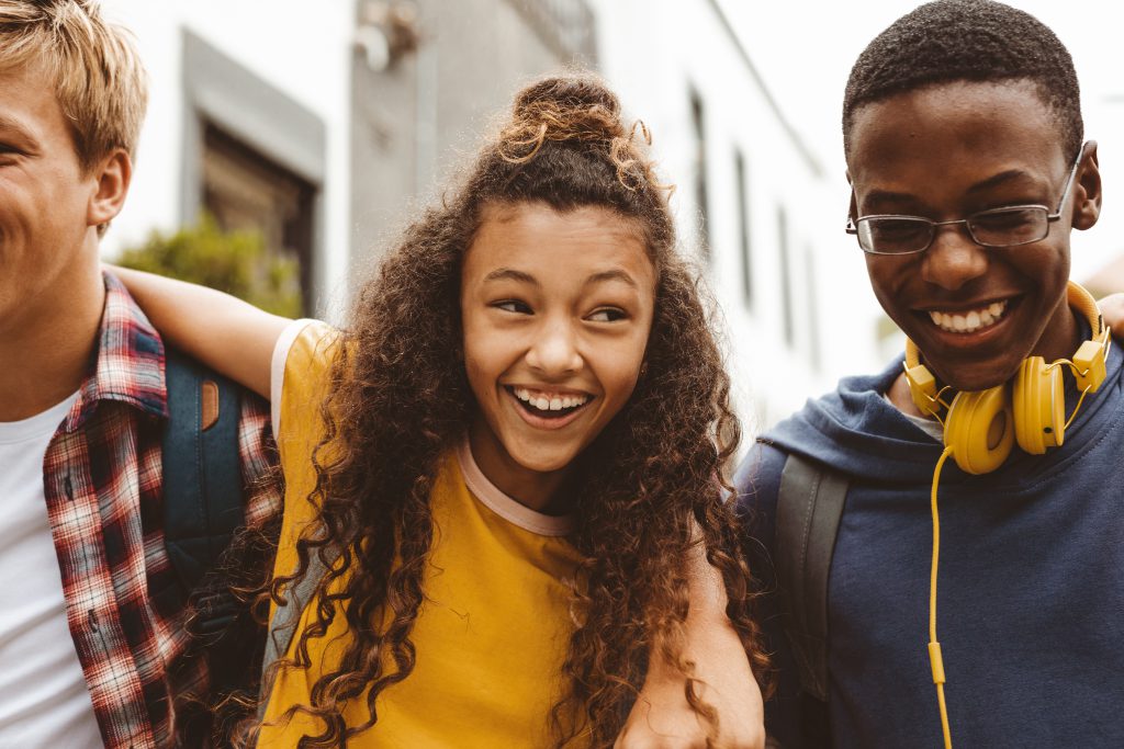 Close up of a smiling teenage girl standing outdoors with college friends. Group of multiethnic boys and a girl having fun standing outdoors with arms around each other.