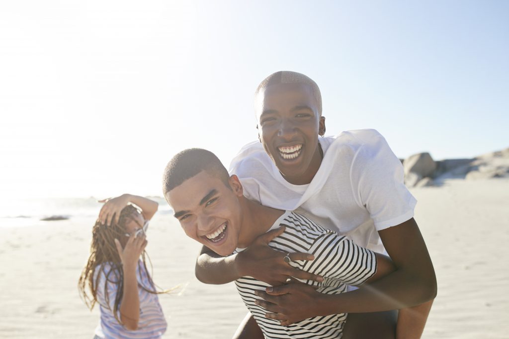 Excited man piggybacking friend with woman in background at beach