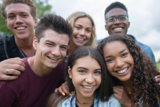 A multi-ethnic group of university and college students stop to pose for a group portrait.  They are huddled together closely and all dressed casually as they smile and enjoy the moment.
